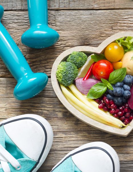 shoes, weights, fruit in a heart bowl on wood plank background